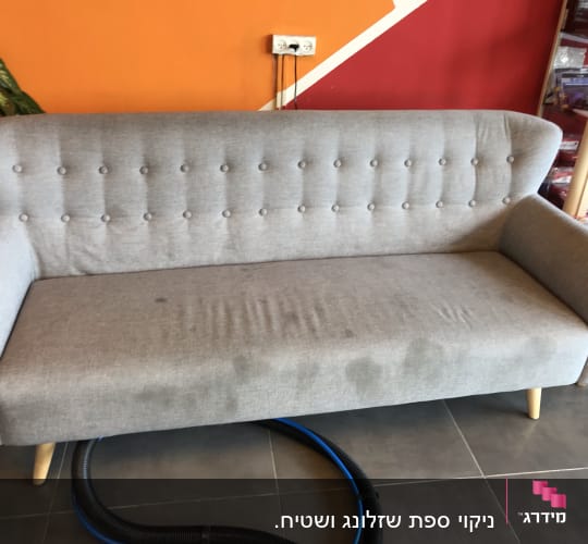 ספה אפורה עם כתמים וצינור ניקוי על הרצפה